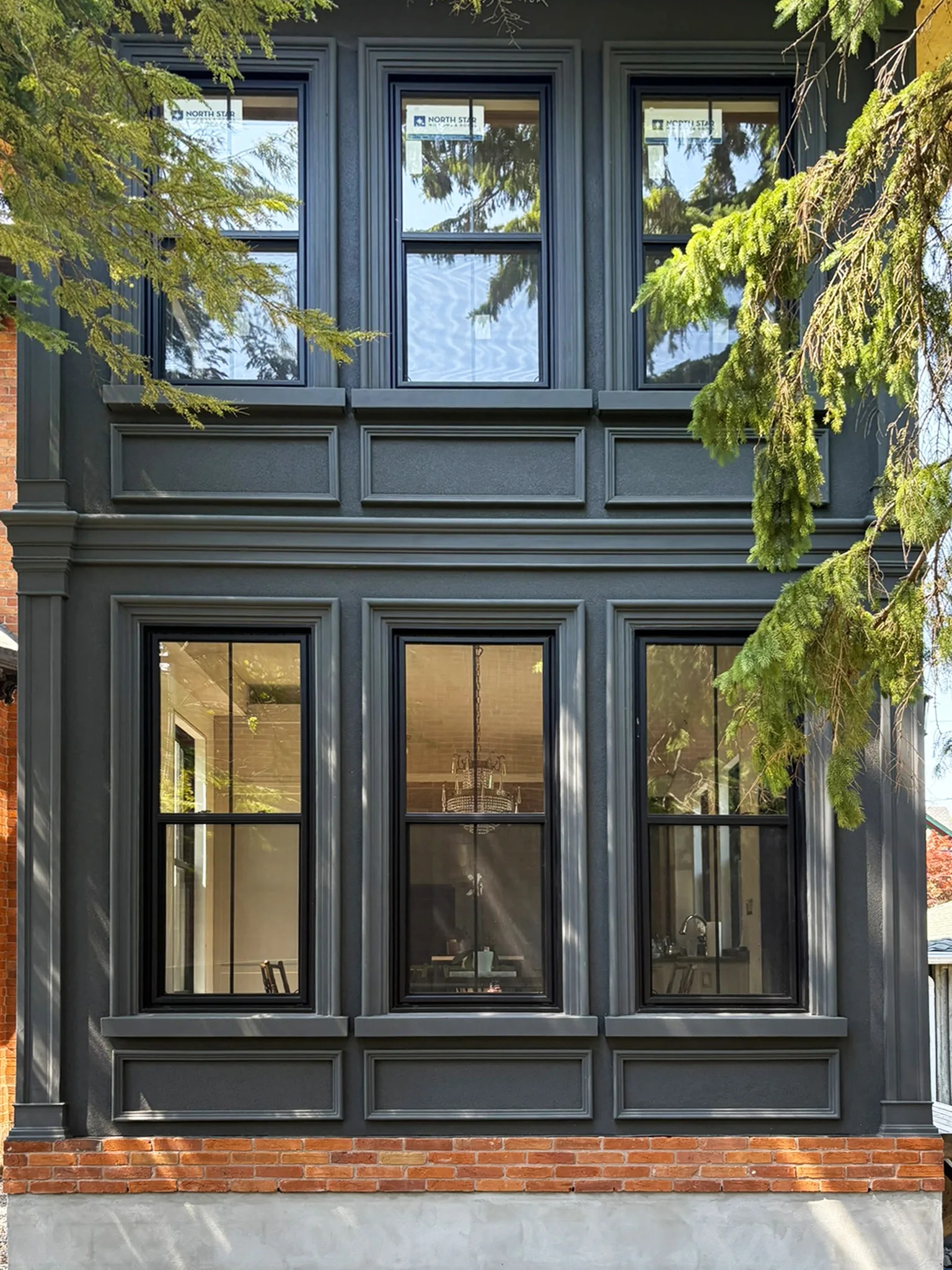 Dark-painted historic home exterior with detailed window trim and brick foundation